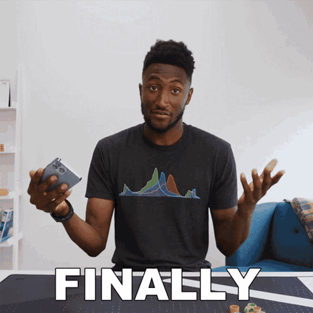 a man in a black shirt is holding a cell phone in front of a table that says finally on it