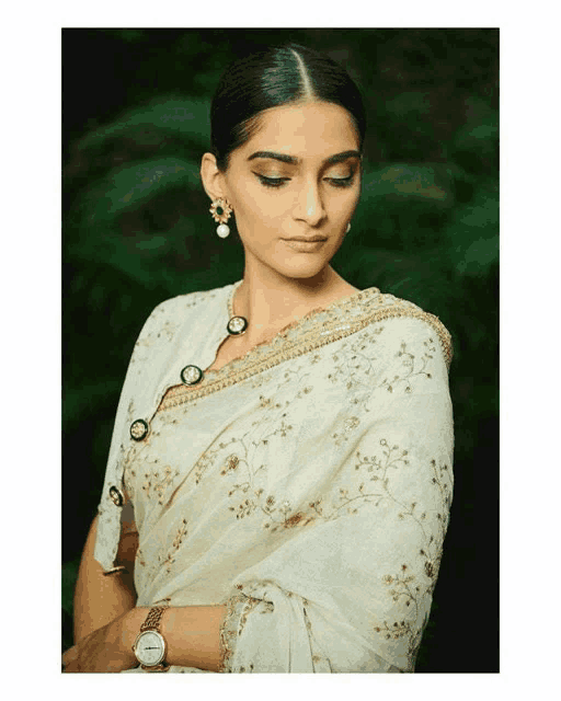 a woman wearing a white embroidered blouse and earrings is wearing a watch