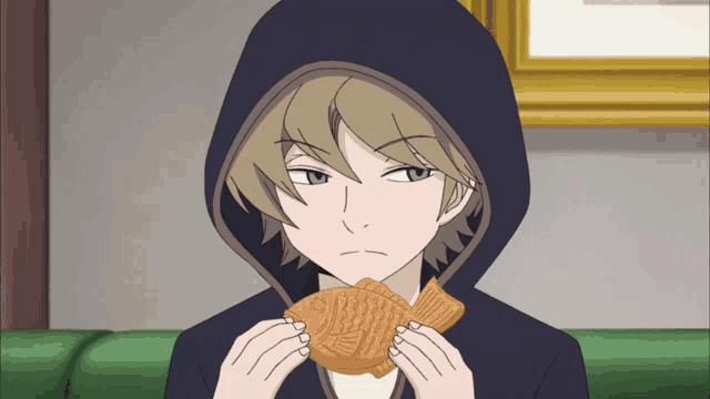 a man in a hooded jacket is eating a fish shaped pastry