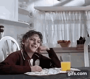 a young boy is sitting at a table with a glass of orange juice and a plate of food .