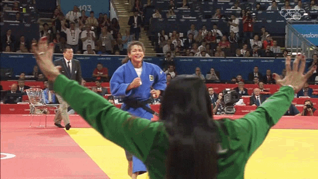 a woman in a green shirt stands in front of a judo match with the number 103 on the wall behind her