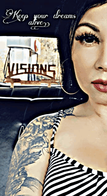 a woman with a tattoo on her arm is sitting in a car with a sign that says visions in the background