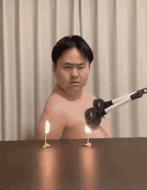 a man without a shirt is sitting at a table with candles on it