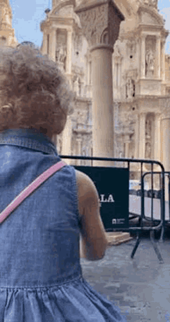 a little girl in a blue dress is standing in front of a building with a sign that says la