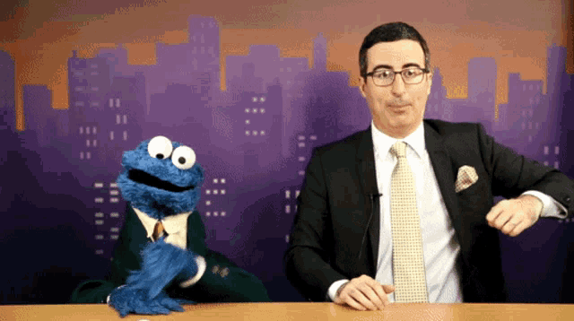 a man in a suit stands next to a cookie monster puppet