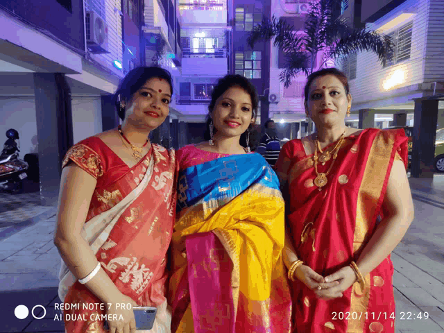 three women posing for a picture with a redmi note 7 pro in the background