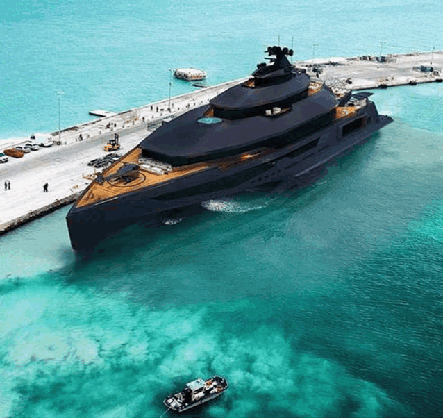 an aerial view of a large black yacht in the ocean next to a small boat .