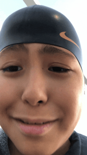 a young boy wearing a nike swim cap looks at the camera