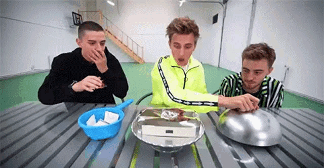 a group of young men are sitting at a table with a bowl , pan , and a tray .