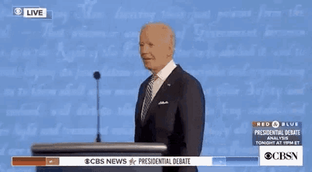 a man in a suit and tie is giving a speech at a podium in front of a wall of text .