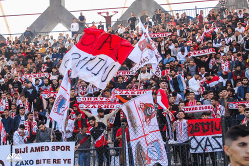 a crowd of people in a stadium holding flags and a sign that says biji amed spor zaxo bite re ye