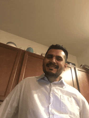 a man with a beard wearing a white shirt smiles in front of wooden cabinets