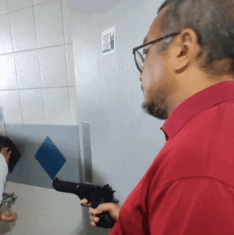 a man in a red shirt and glasses is holding a gun