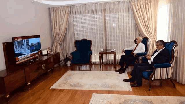 two men sit in chairs in front of a tv which says istanbul on the screen