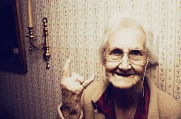 an elderly woman wearing glasses and earrings is giving a middle finger .