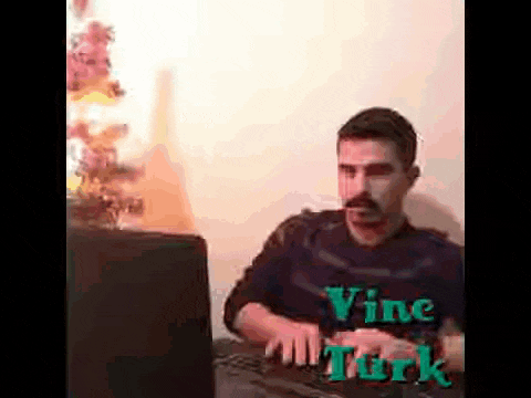 a man with a mustache is sitting at a desk using a computer .