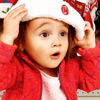 a little girl wearing a santa hat and a red jacket with a surprised look on her face