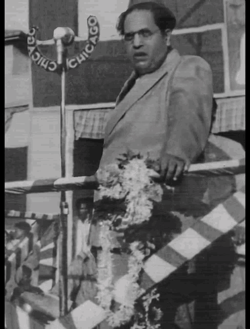 a black and white photo of a man speaking into a microphone with the word chicago on the wall behind him