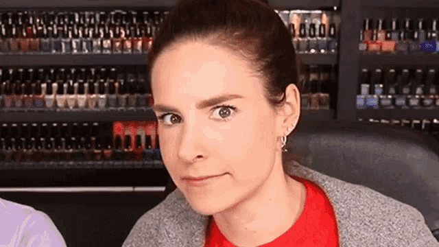 a woman in a red shirt is making a funny face in front of a shelf full of nail polish