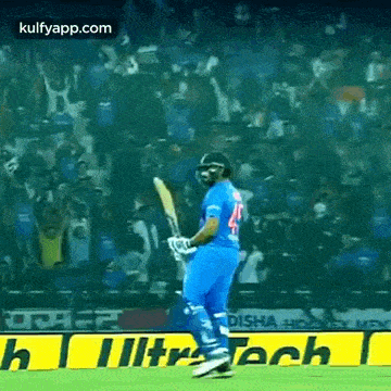 a cricket player is walking on a field with a bat in his hand in front of a crowd .