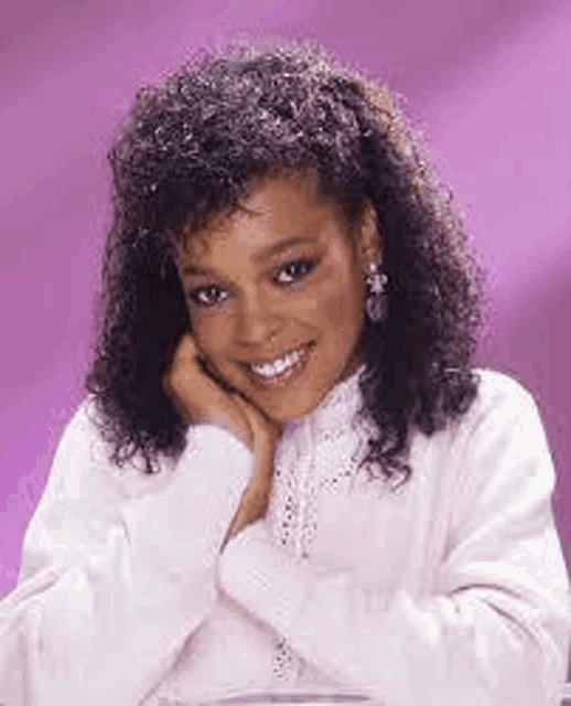 a woman with curly hair is wearing a white sweater and earrings and smiling .