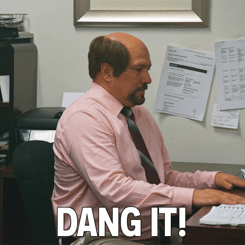 a man in a pink shirt and tie sits at a desk with dang it written on the bottom right