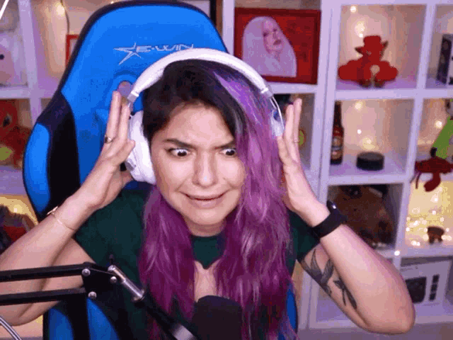 a woman with purple hair is wearing headphones and a blue gaming chair