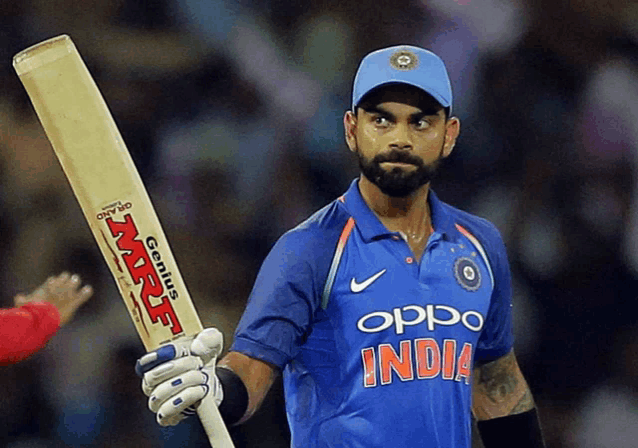 a man in a blue shirt that says india holds up his bat