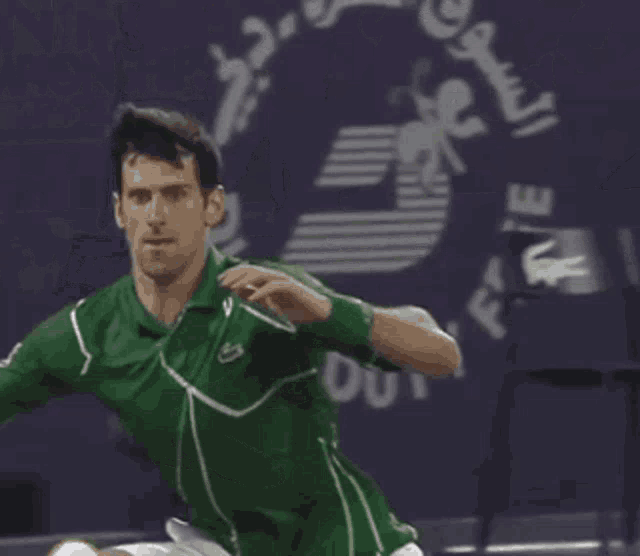 a man in a green shirt and white shorts is stretching on a tennis court in front of a sign that says lacoste