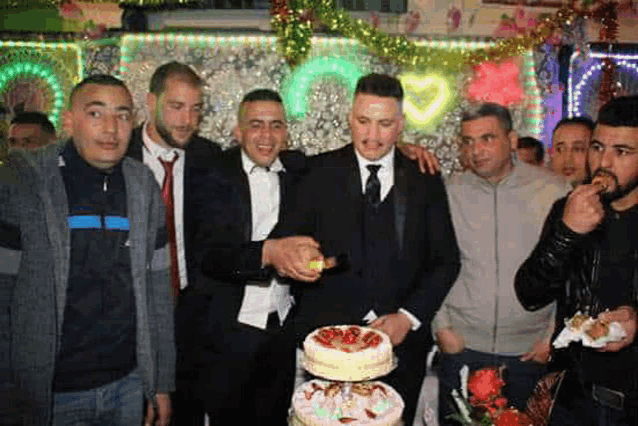 a group of men are posing for a picture while a man cuts a cake .