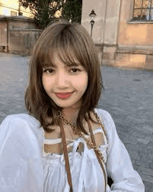 a woman is taking a selfie in front of a building while wearing a white top and a brown purse .