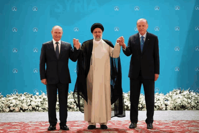 three men are holding hands in front of a blue wall with the word syria on it