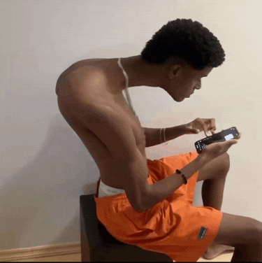 a shirtless man in orange shorts is looking at his cell phone