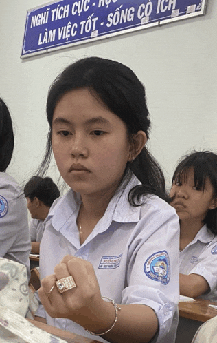 a girl wearing a ring sits in front of a sign that says nghĩ tích cục