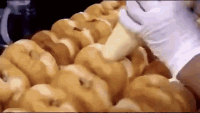 a person is making a bunch of donuts in a bakery with gloves on .