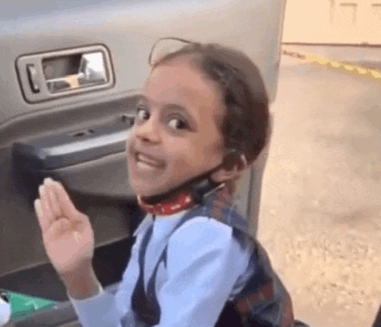 a little girl wearing a headset is sitting in the back of a car and waving .