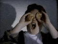 a person is holding a cookie in front of their eyes and screaming .