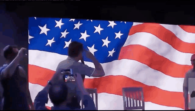 a man salutes in front of an american flag on a screen