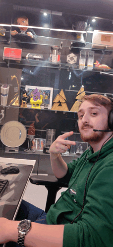 a man wearing headphones and a green sweatshirt giving a peace sign