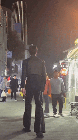 a man in a suit walks down a street at night with a sign that says ' a ' on it