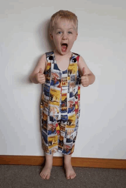 a young boy giving a thumbs up while wearing a jumpsuit that says ' coca cola ' on it