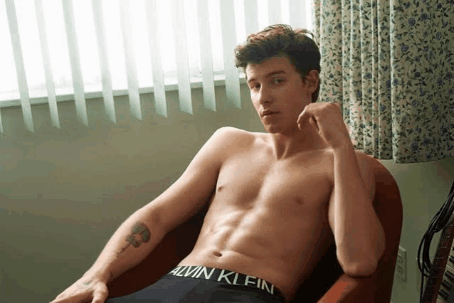 a shirtless man is sitting in a chair with calvin klein underwear on .