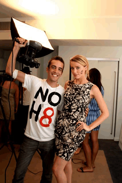 a man wearing a no h8 shirt stands next to a woman in a dress