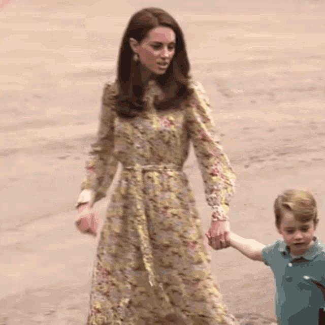 a woman in a floral dress is holding the hand of a young boy in a green polo shirt .