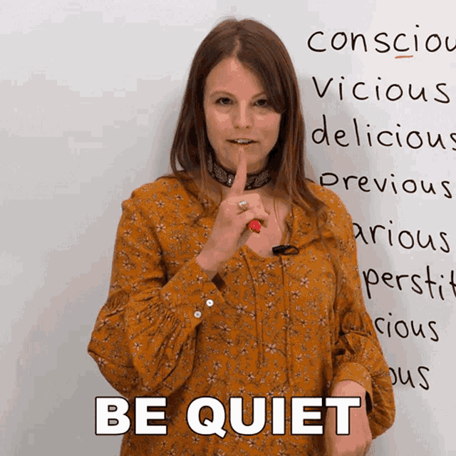 a woman holds her finger to her lips in front of a white board that says " be quiet "