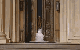 a person is standing in front of a door that is open and a fountain is coming out of it .