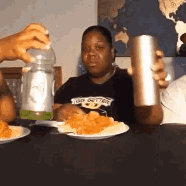 a woman is sitting at a table with a plate of food and a bottle of water and a can of soda .