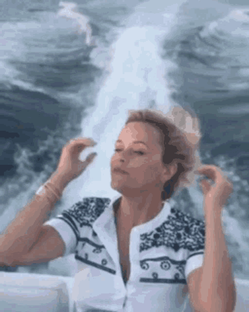 a woman is sitting on a boat in the ocean with her hands in her hair .