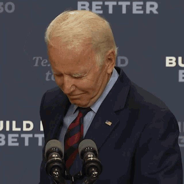 a man in a suit and tie is standing in front of two microphones with the words better behind him