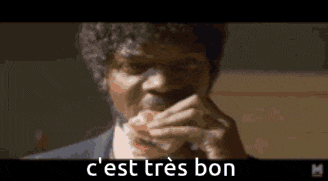 a man with curly hair is eating a sandwich with the words `` c est tres bon '' written on the bottom .